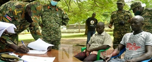 Cpt James Majok, the SSPDF Liaison Officer, signs the repatriation documents at the 4th Division Barracks in Gulu District on 12 October, 2021. Seated are the two rebel suspects, Pte Augustine Yakal (right) , and Cpl Victor Batali. PHOTO | TOBBIAS JOLLY OWINY