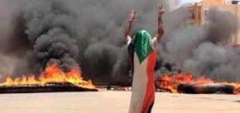 A protester wearing a Sudanese flag flashes the victory sign in front of burning tires and debris on road 60, near Khartoum's army headquarters in Khartoum, June 3, 2019. (AP)